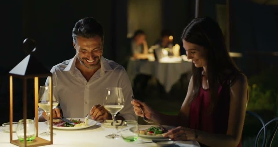 A couple laughing over dinner at an outdoor table at night